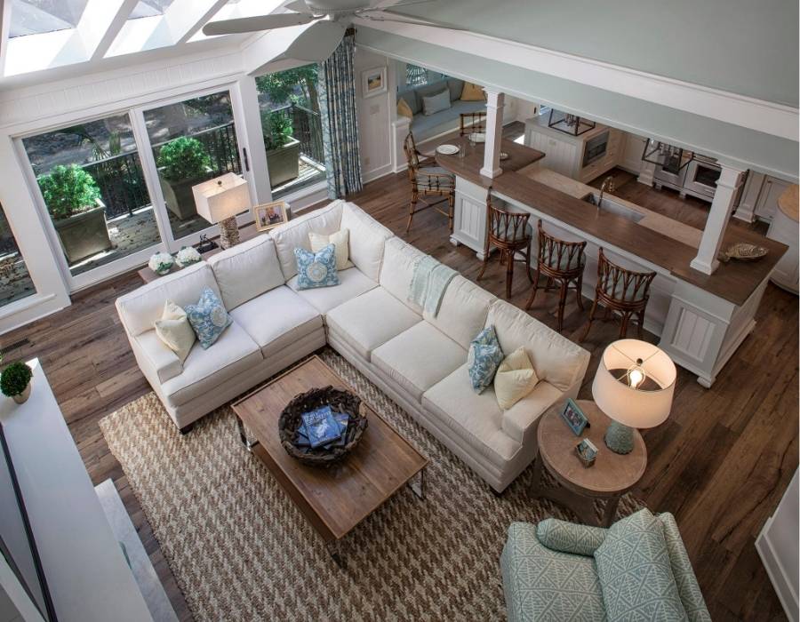 Spacious coastal-style living room with vaulted ceilings, white sectional sofa, hardwood floors, large windows, and open-concept kitchen with bar seating.