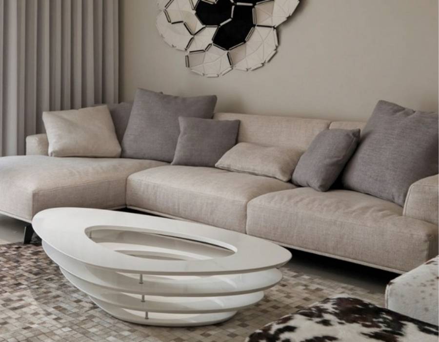 Modern living room with custom beige upholstered sectional sofa, gray accent pillows, abstract wall art, and contemporary oval white coffee table on a textured rug.